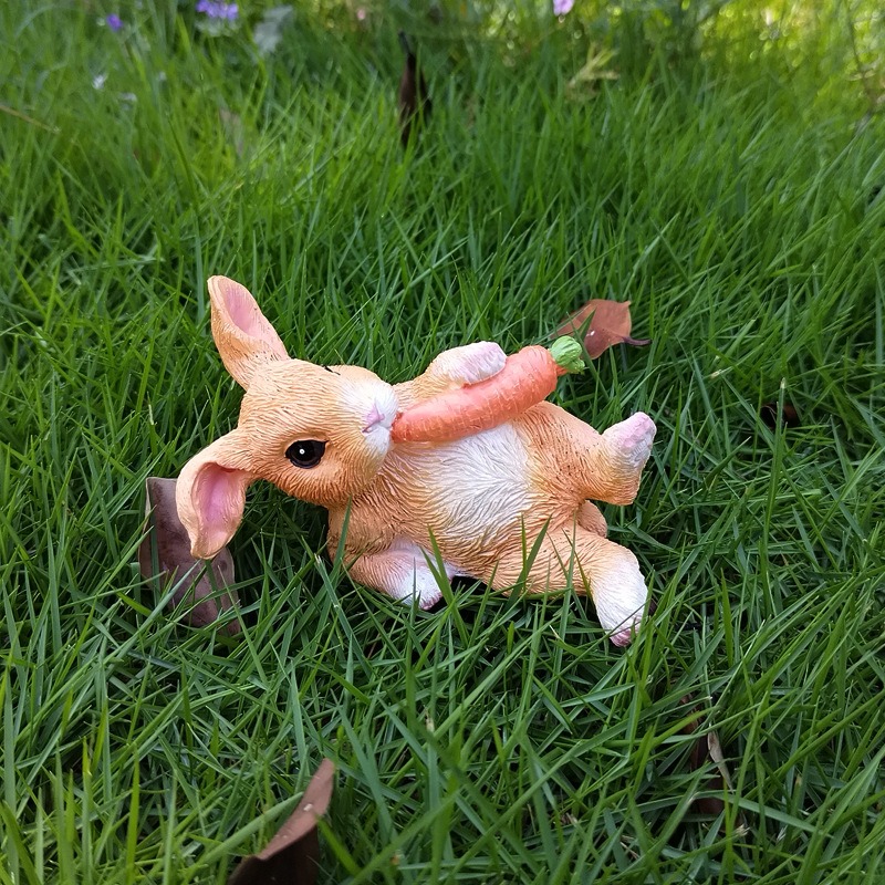 Reclining rabbit gnawing a large carrot on green grass