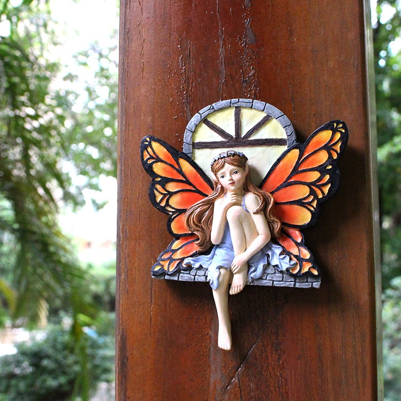 Fairy ornament mounted on a wooden post among green garden foliage