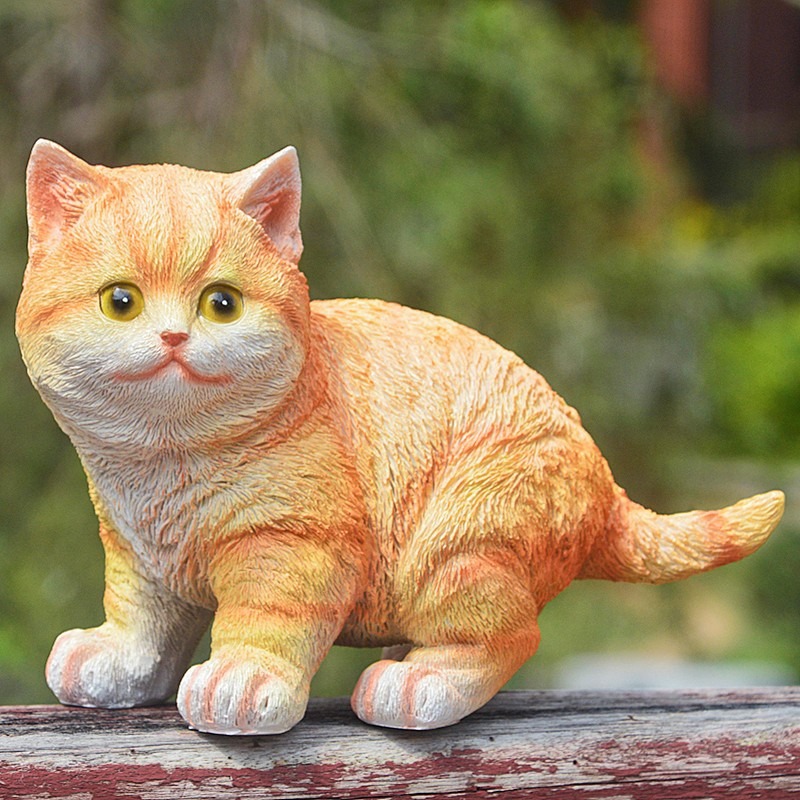 Orange tabby cat statue perched on a weathered wooden rail outdoors