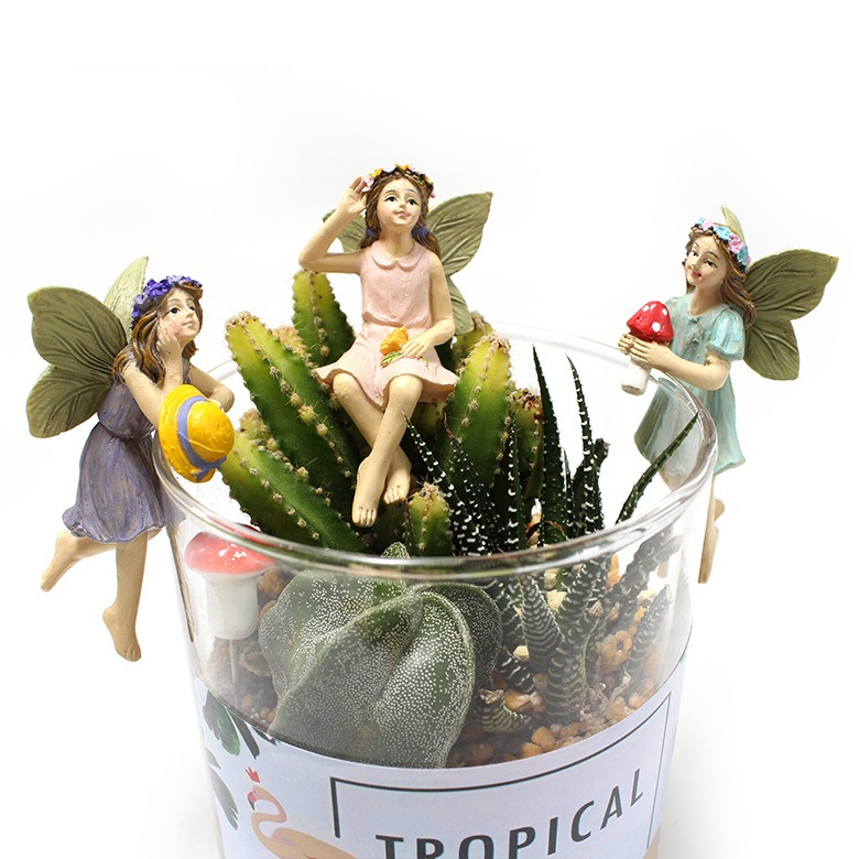 Fairy figurines perched on the rim of a glass planter with cactus