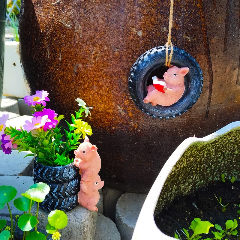 Pig figurine peeking from a hanging tyre decoration beside a planter