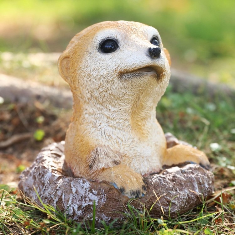 Meerkat ornament peeking from rock among green garden plants