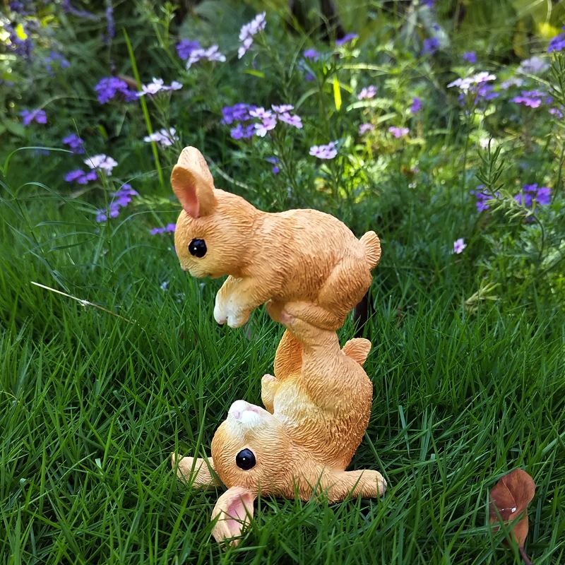 Stacked resin rabbit ornaments placed on green grass beside purple flowers