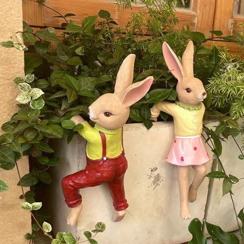 Two bunnies clinging to a grey concrete planter beside green ivy
