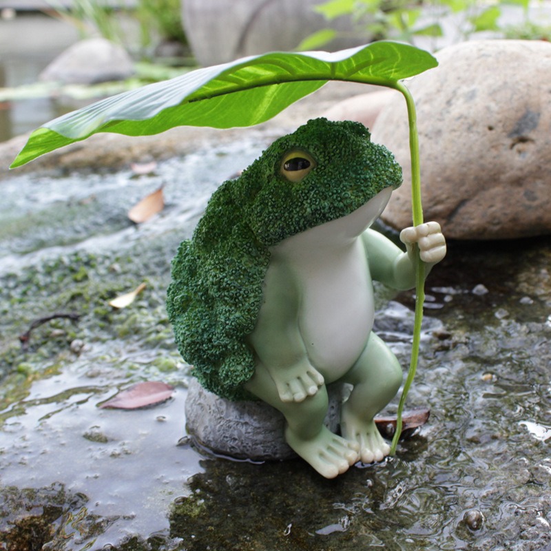 Frog figurine beside a pond rock with moss and water nearby