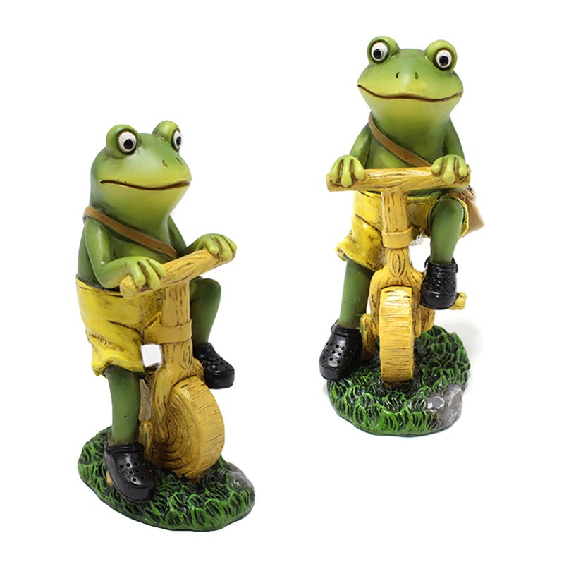 Two frog figurines on bikes sitting in a grass-textured base