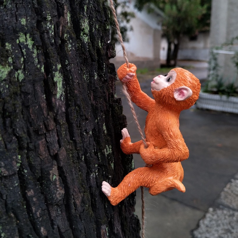 Monkey and squirrel figurines hanging from a tree trunk in a garden