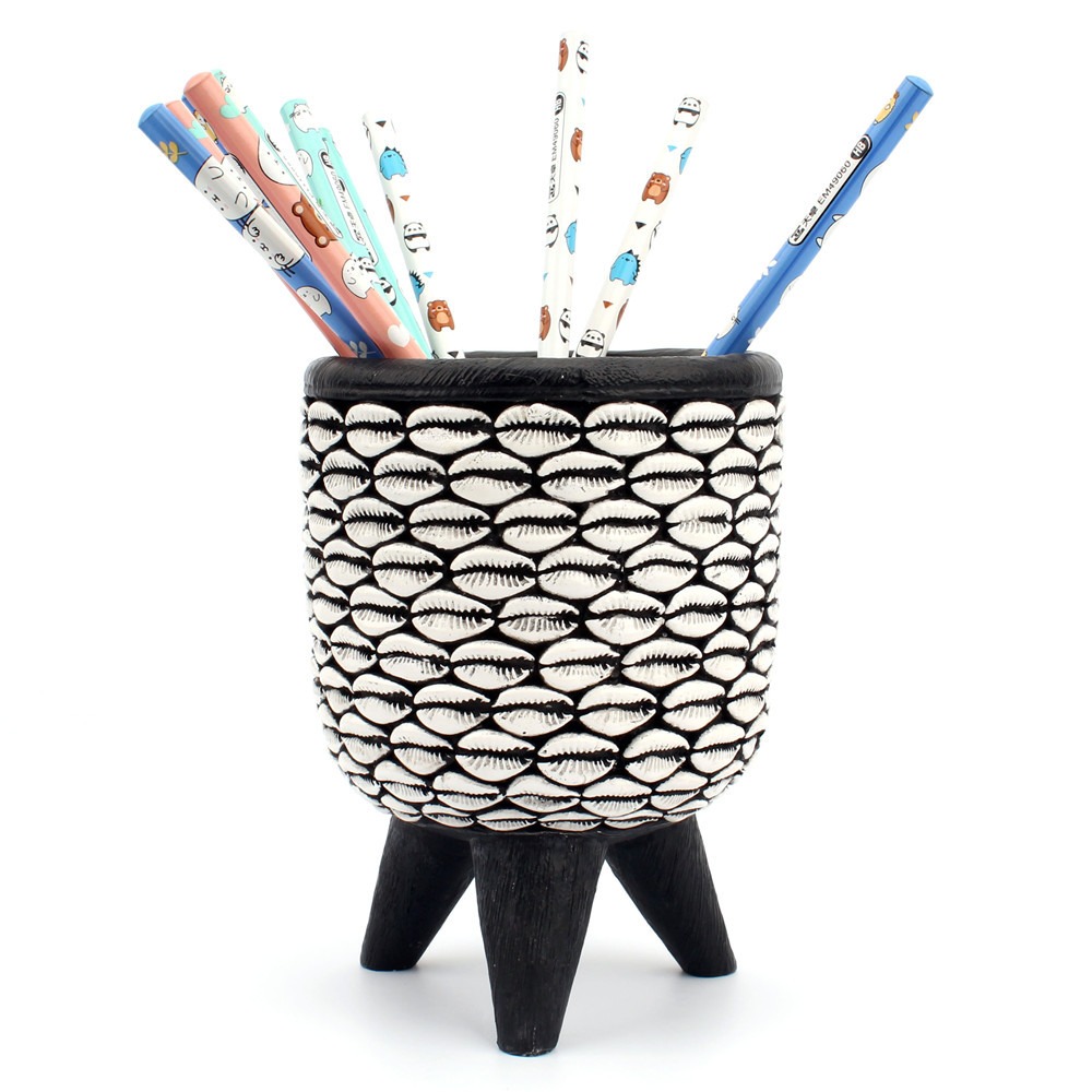 Cowrie shell tube filled with pencils and pens standing upright on a desk