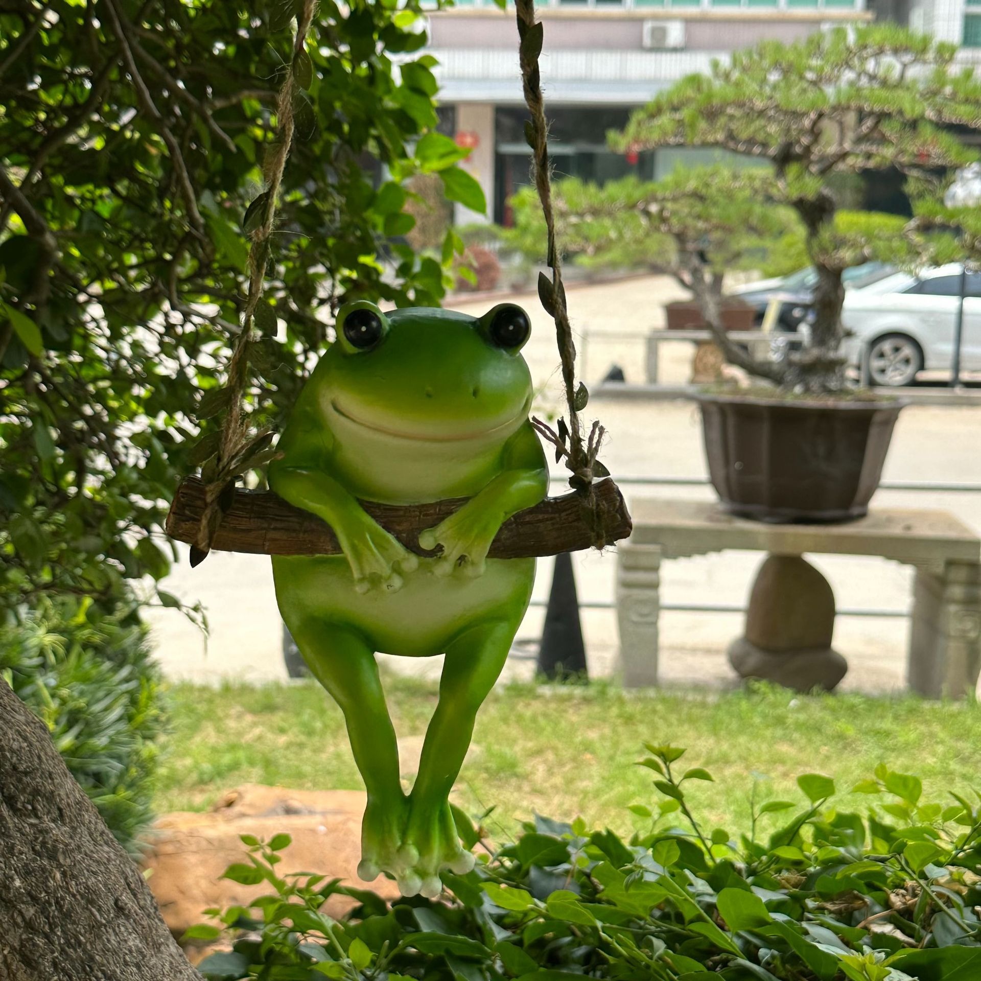 Green frog figurine swinging in leafy garden tree at a relaxed angle