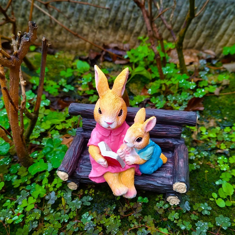 Rabbit reading figurine sitting on log bench among clover and moss