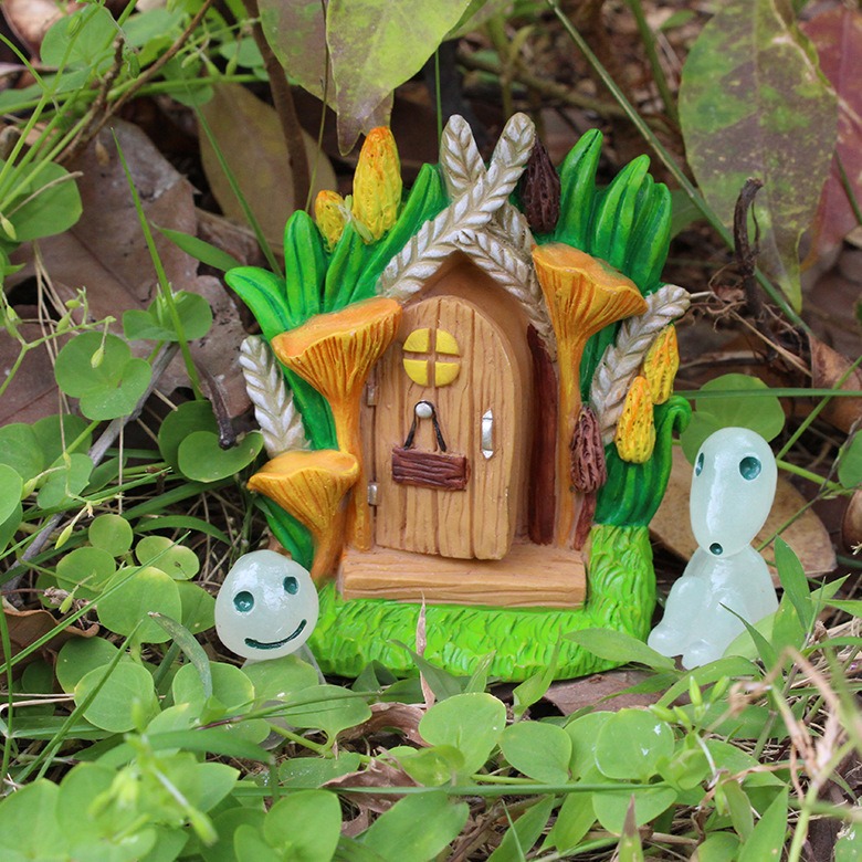 Fairy door framed by mushrooms and wheat among green leaves
