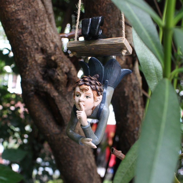 Elf hanger dangling from a wooden swing against tree bark and green leaves