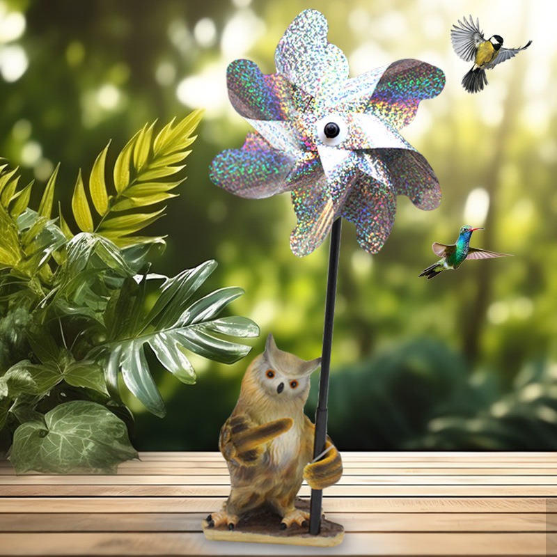 Owl pinwheel garden stake on wooden deck with plants in background