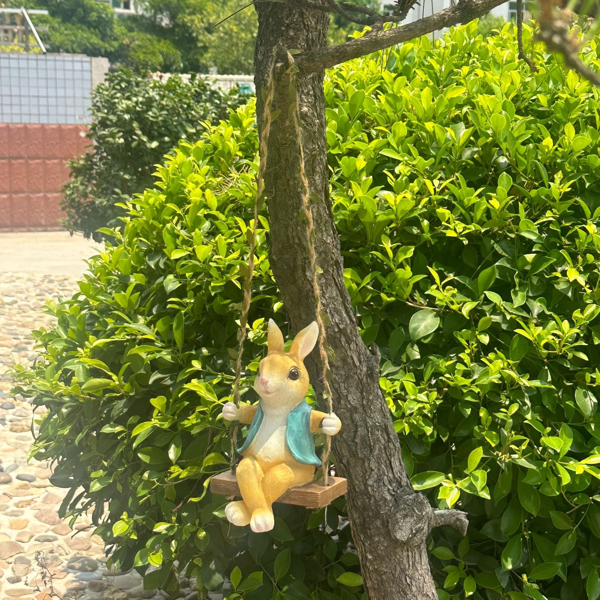 Rabbit figurine in a teal vest on a rope swing beside tree trunk