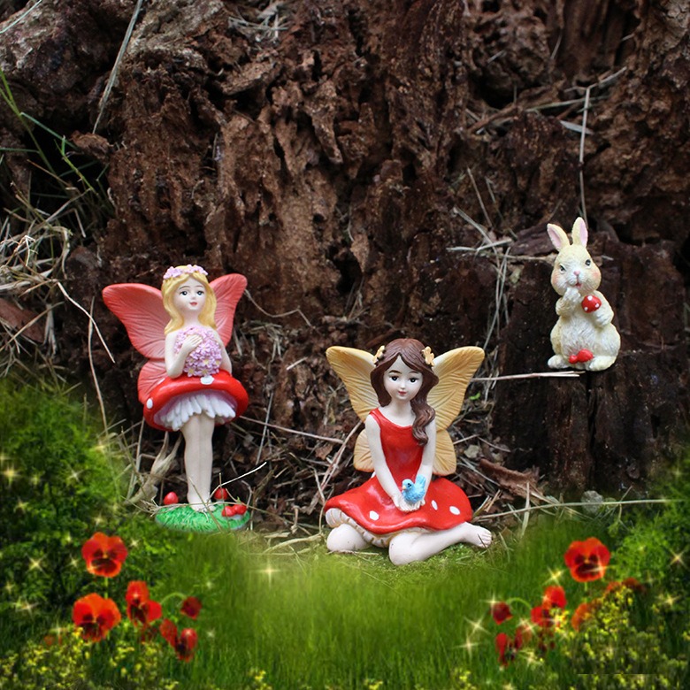 Fairy figurines nestled among red flowers and grass beside a tree stump