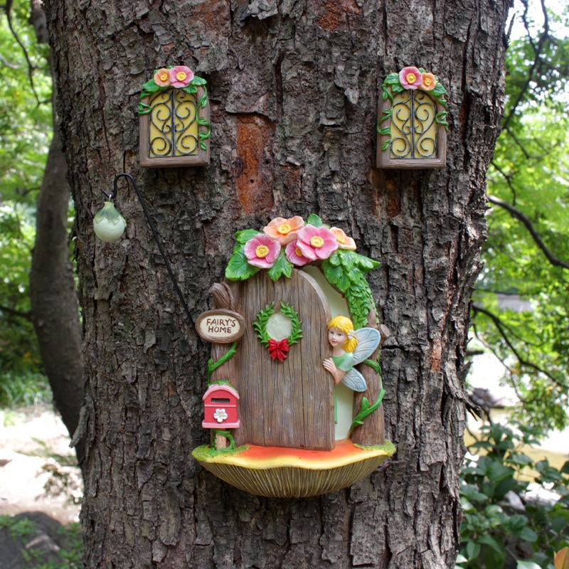 Fairy door with arranged windows and hanging lantern on a green tree trunk