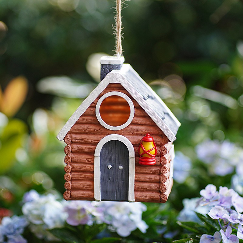 Bird house hanging on jute cord among hydrangeas with arched door visible