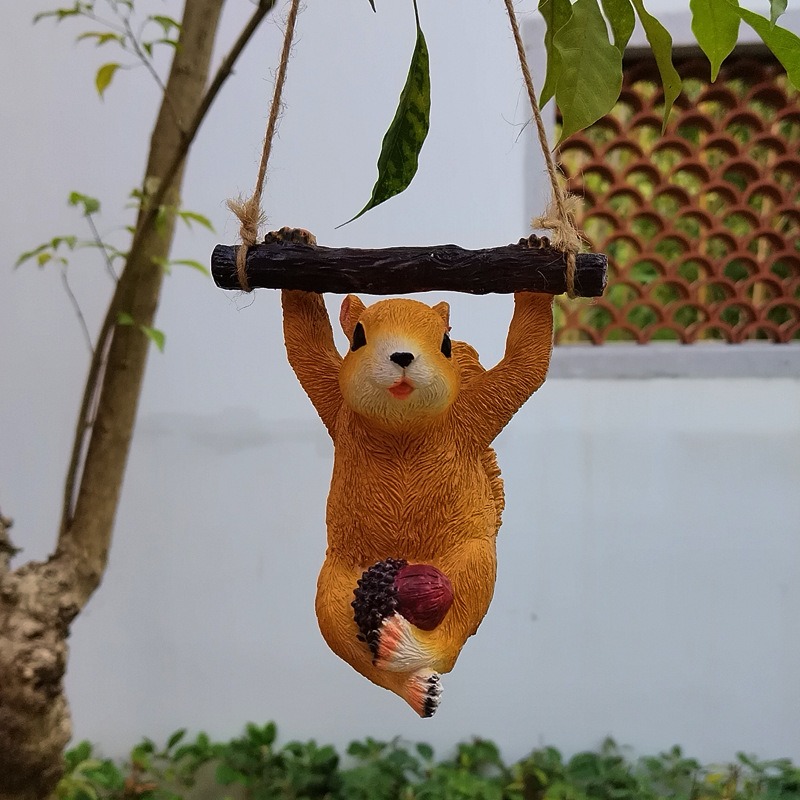 Resin squirrel hanging from a garden branch among green foliage