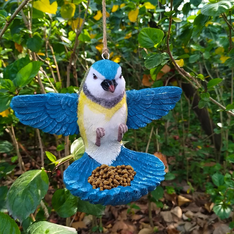 Blue tit ornament hanging in a tree with seed in its tray