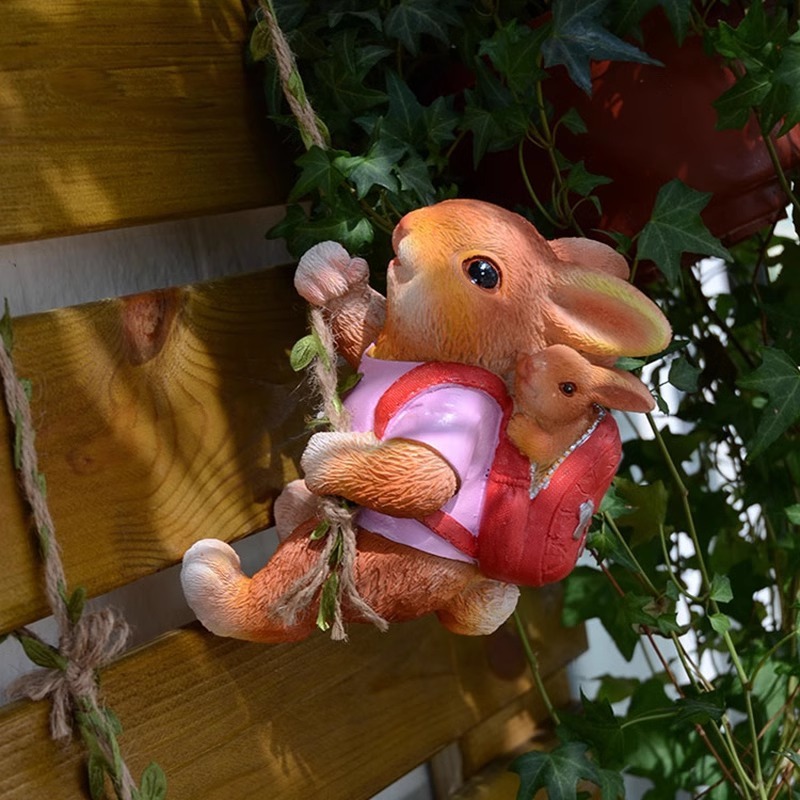 Brown rabbit figurine hanging on a wooden fence beside green ivy