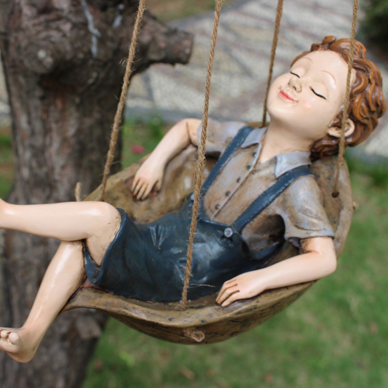 Resin boy figurine hanging from jute ropes beside a tree trunk