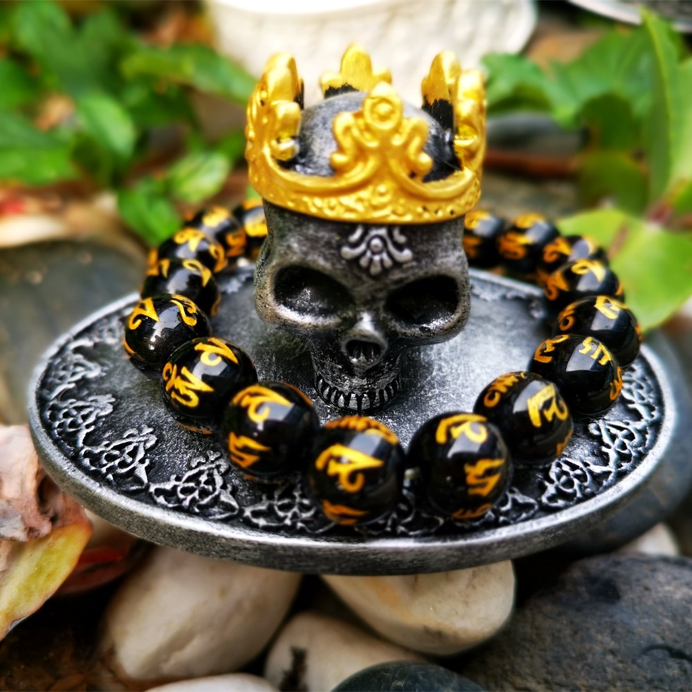 Gold-crowned skull lid beside black beaded bracelets arranged on stones outdoors