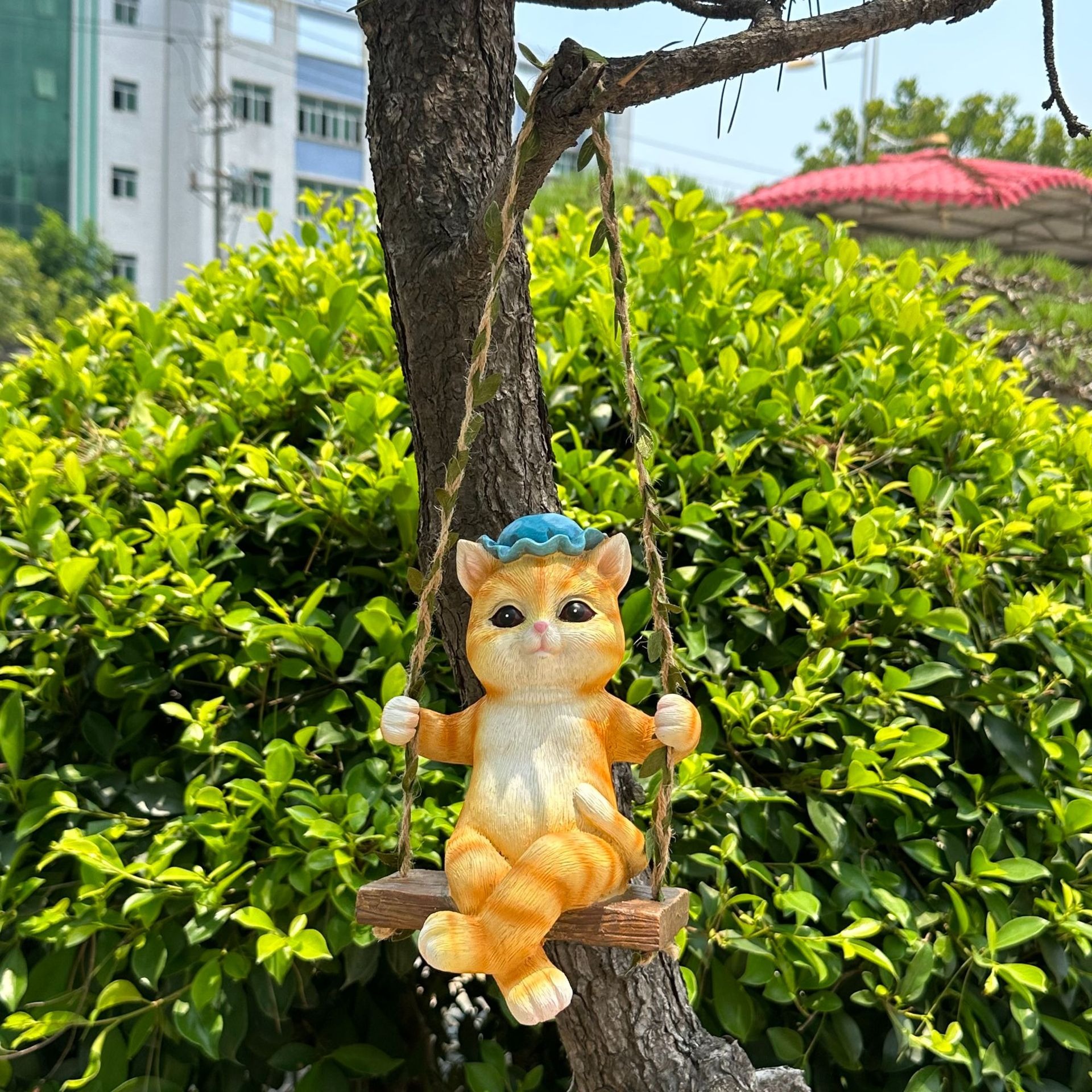 Orange cat figurine with blue hat on a swing hanging from a branch