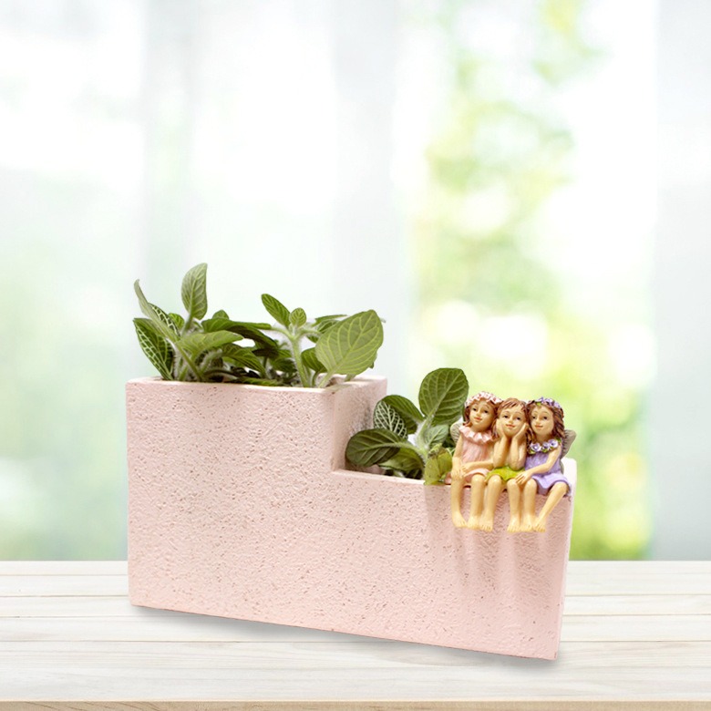 Stepped pink planter holding a leafy plant with a fairy seated on the edge
