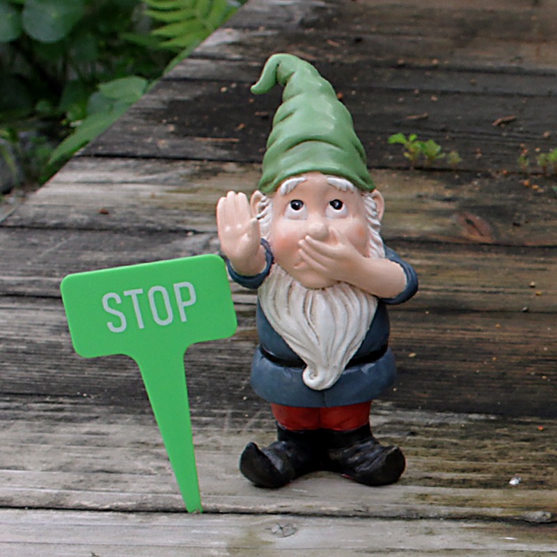 Gnome beside green STOP stake pushed into a wooden deck