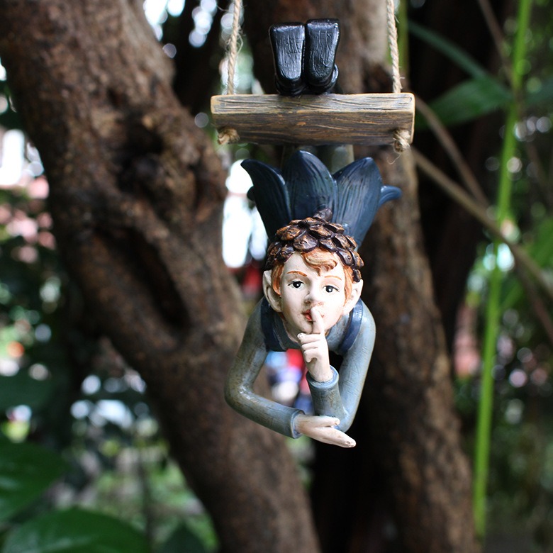 Elf hanger with finger-to-lips pose hanging from a garden tree trunk