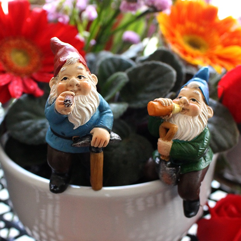 Close-up of two gnomes sitting on a white pot rim with painted faces