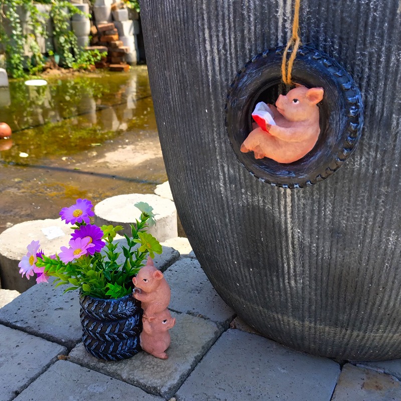 Pig ornament on a gray ribbed planter beside a courtyard flower planter