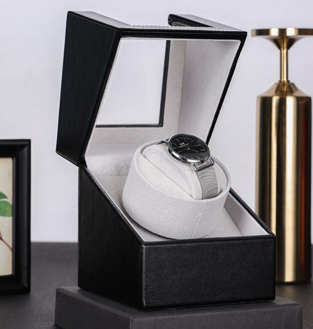 Grey suede lined watch winder on a styled desk beside a gold vase