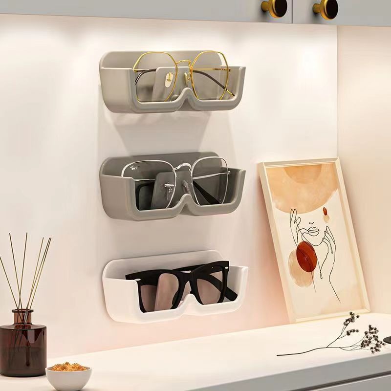 Three stacked grey and white wall holders with sunglasses and eyeglasses above a sideboard