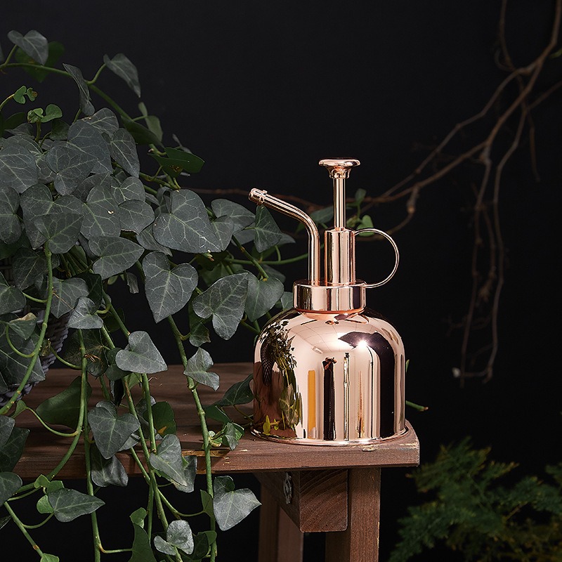 Rose gold plant mister on a wooden stool beside ivy