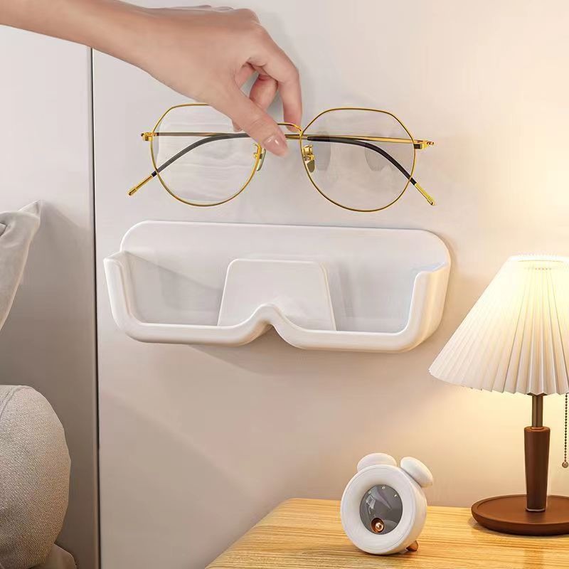 Hand placing gold-framed glasses onto a white wall holder beside a bedside lamp
