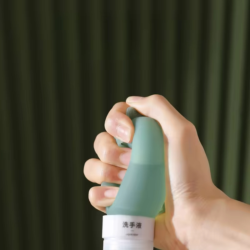 Hand gripping a sage green silicone bottle filled with liquid soap