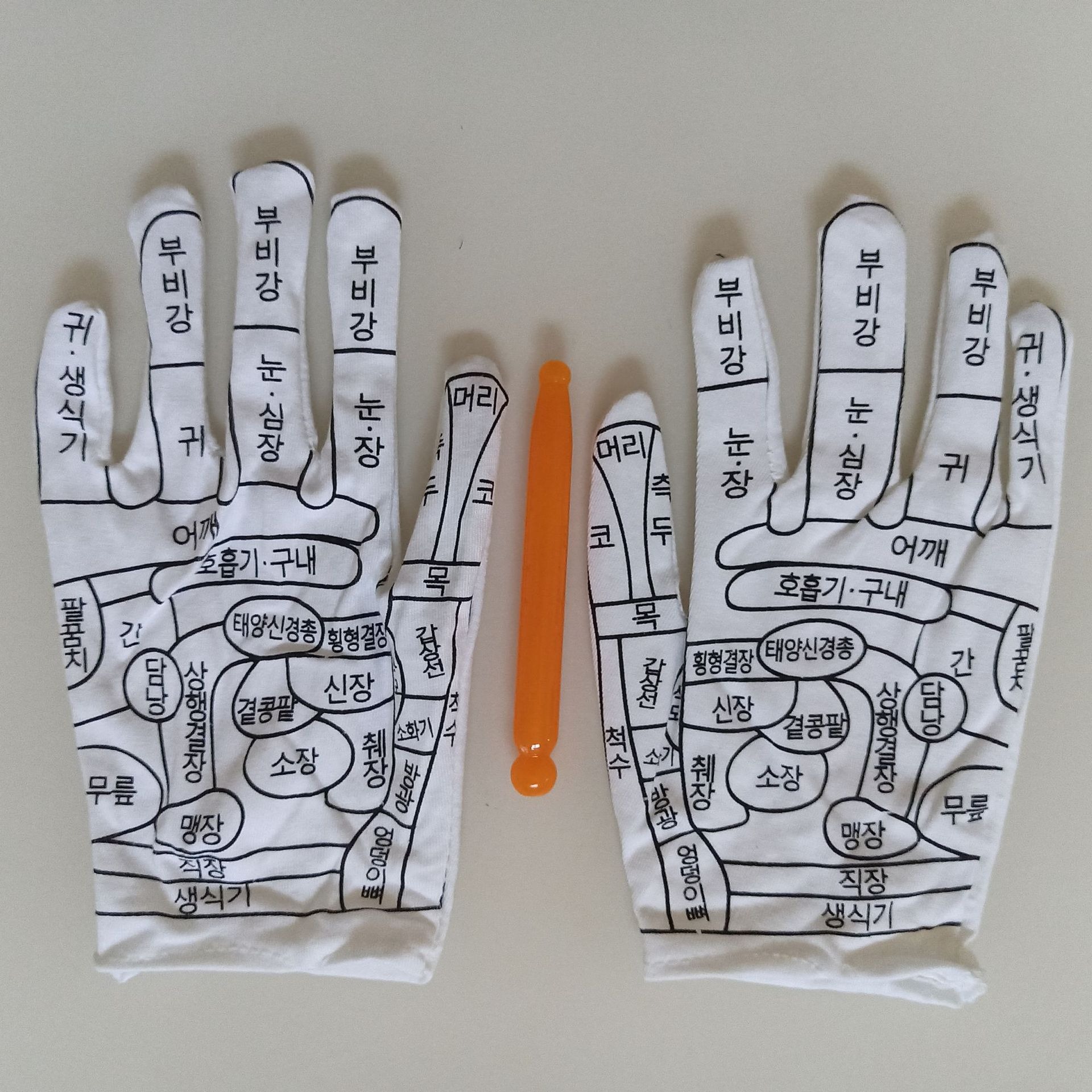 Close-up of glove with Korean text meridian labels alongside orange massage stick tool