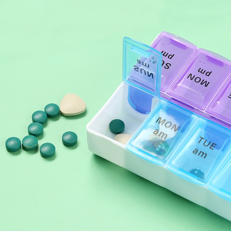 Open morning compartment of pill organizer beside green tablets and a cream capsule