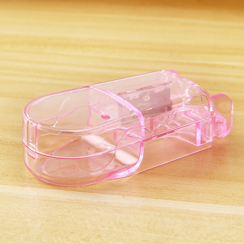 Pink transparent pill cutter on a wooden table showing the internal blade