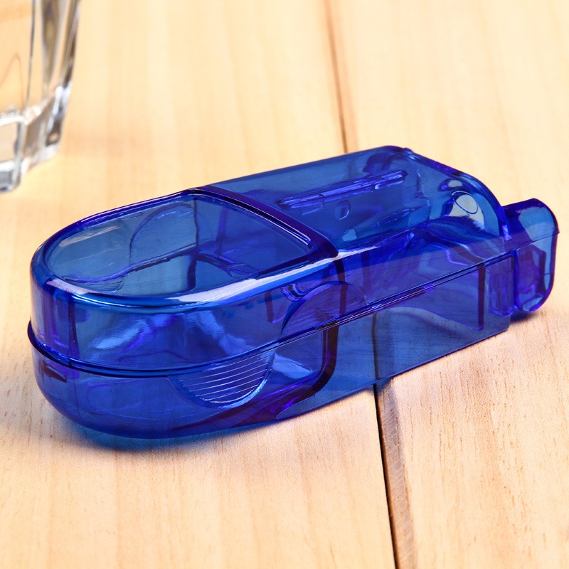 Blue pill cutter on a wooden table beside a drinking glass