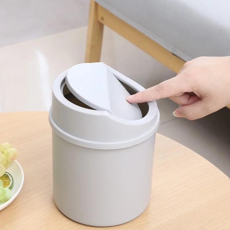 Hand pressing the lid of a grey mini trash can on a wooden table