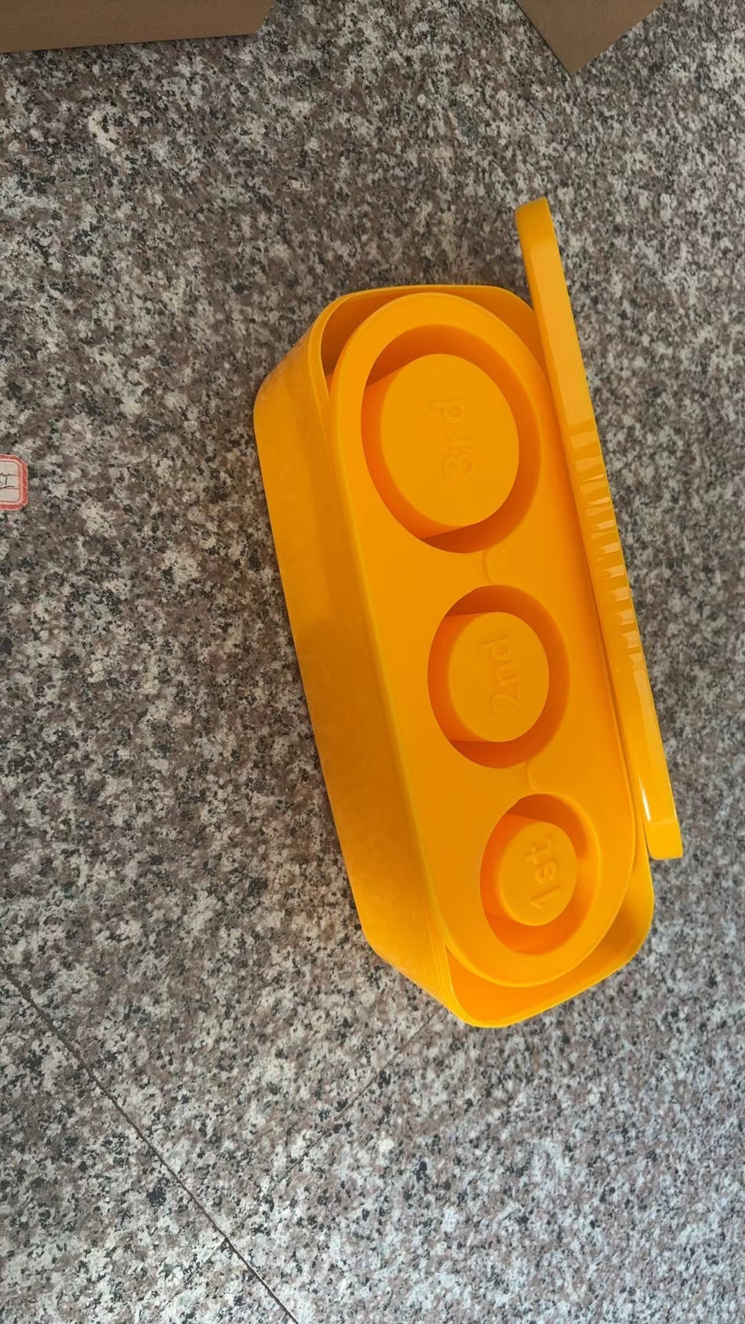Mustard yellow ice grid mold on a granite counter with the lid partly off