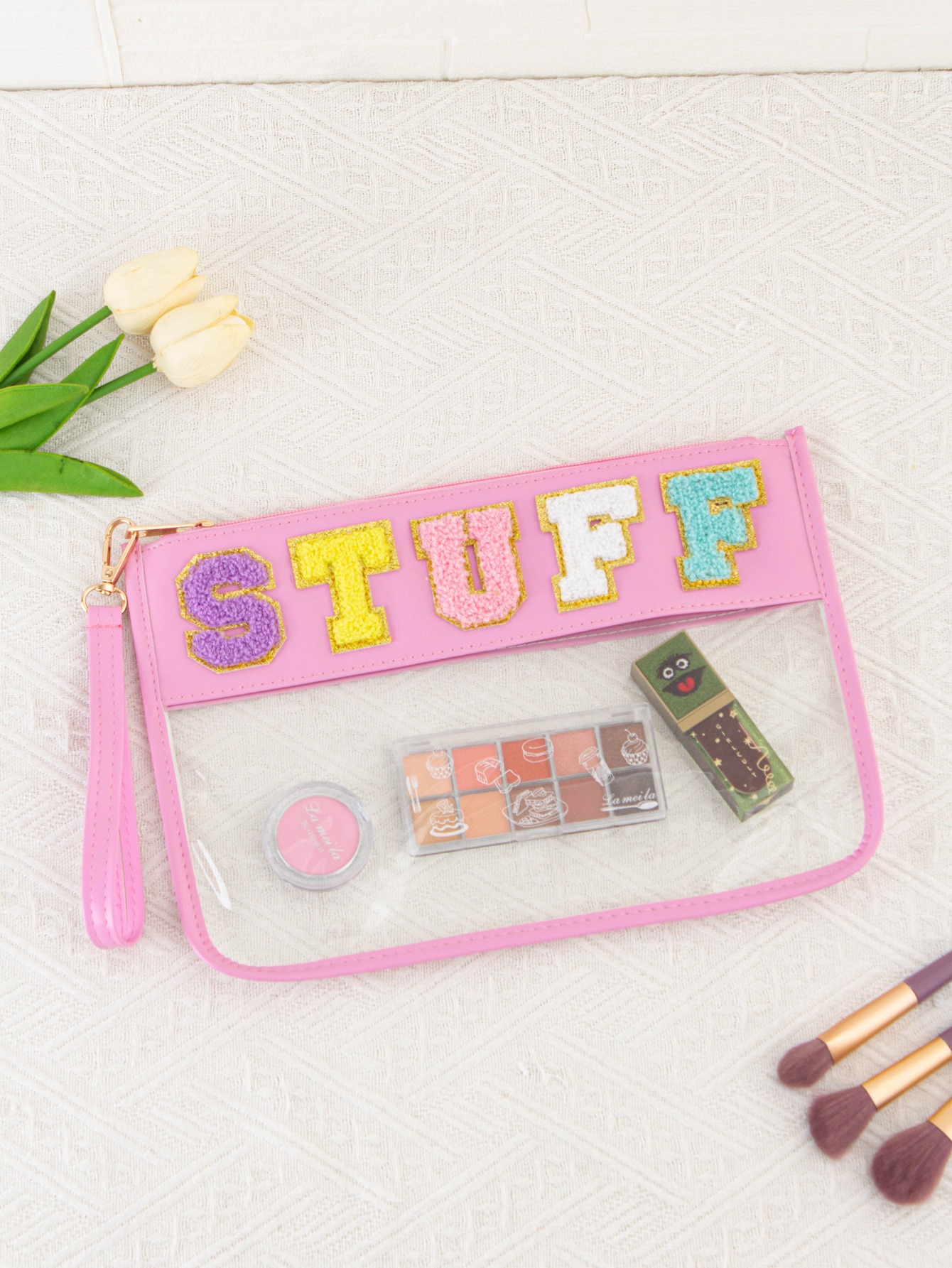 Pink clear zip pouch with chenille letters holding eyeshadow, blush and lipstick