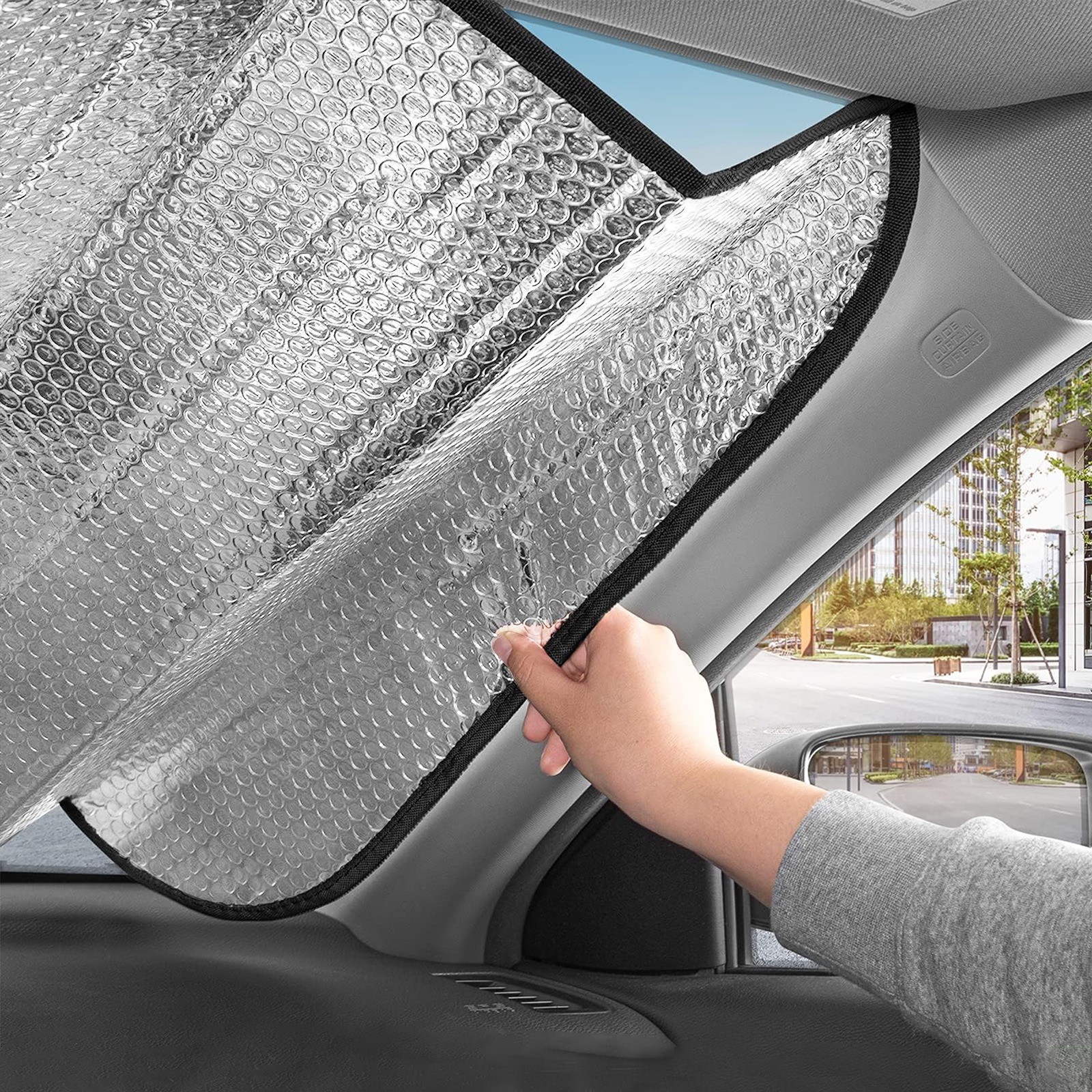 Installing silver car sun shade on windshield to protect car interior from sun
