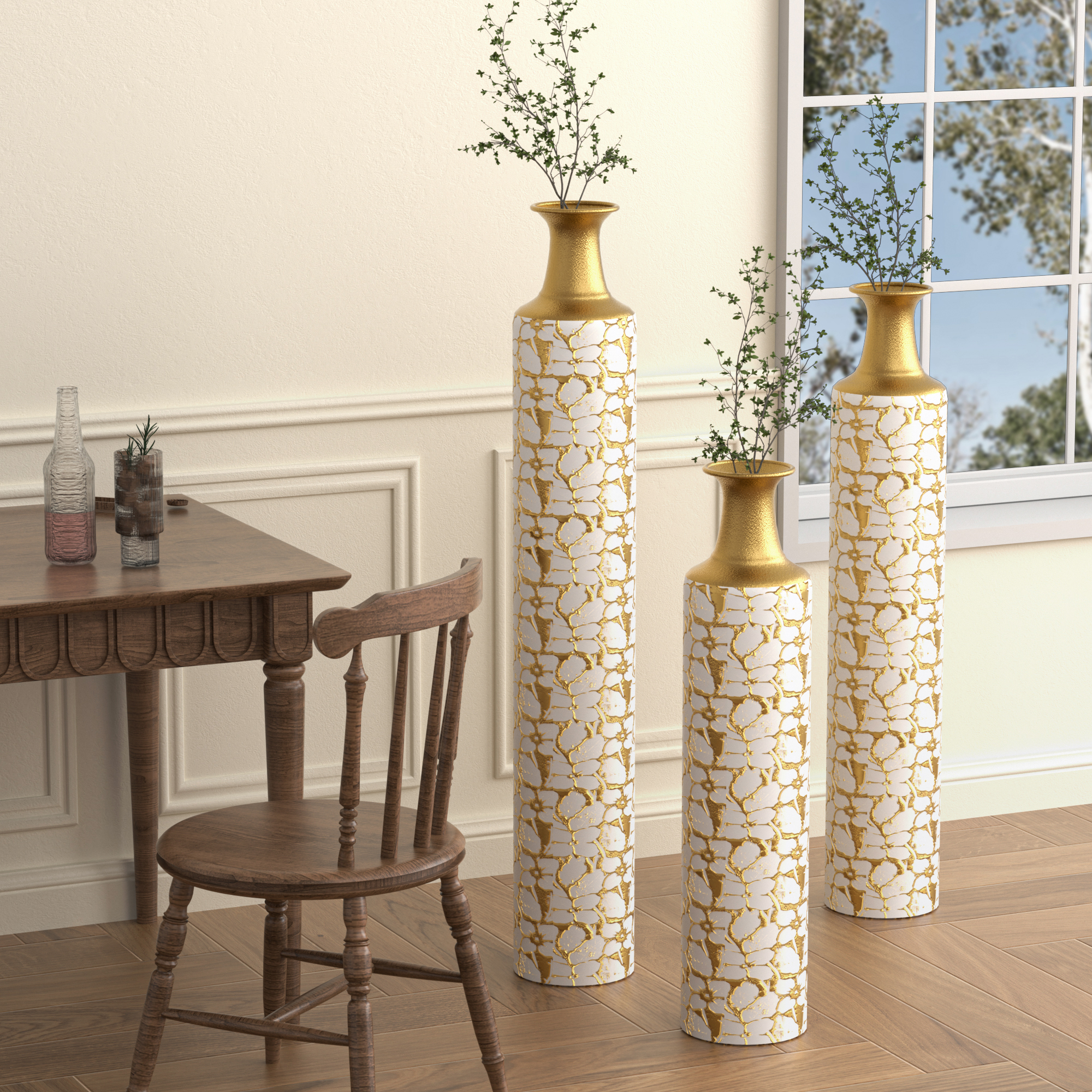 Three gold and white vases with green branches by a dining table