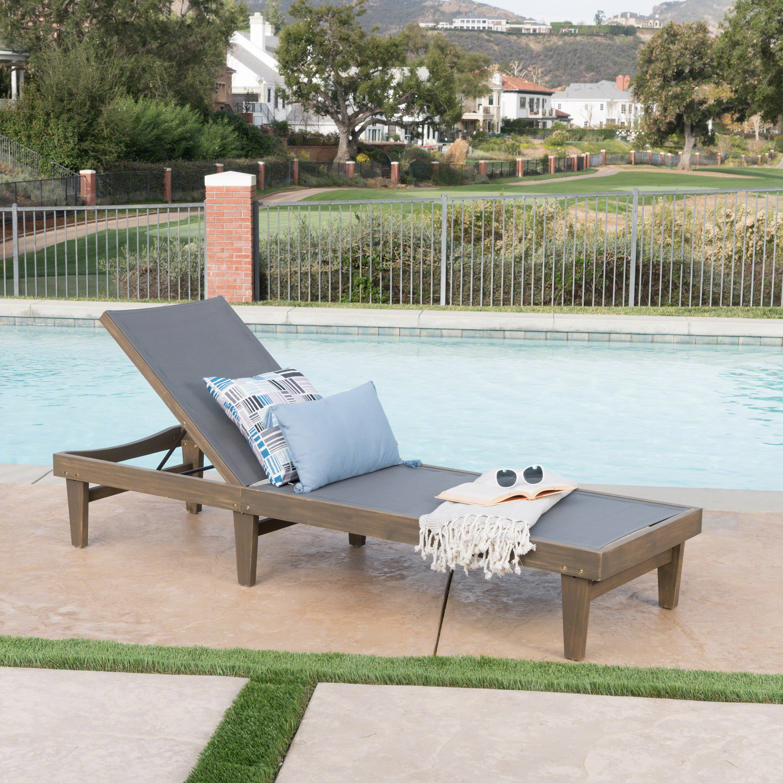 Chaise lounge by a pool with a book and sunglasses on the mesh