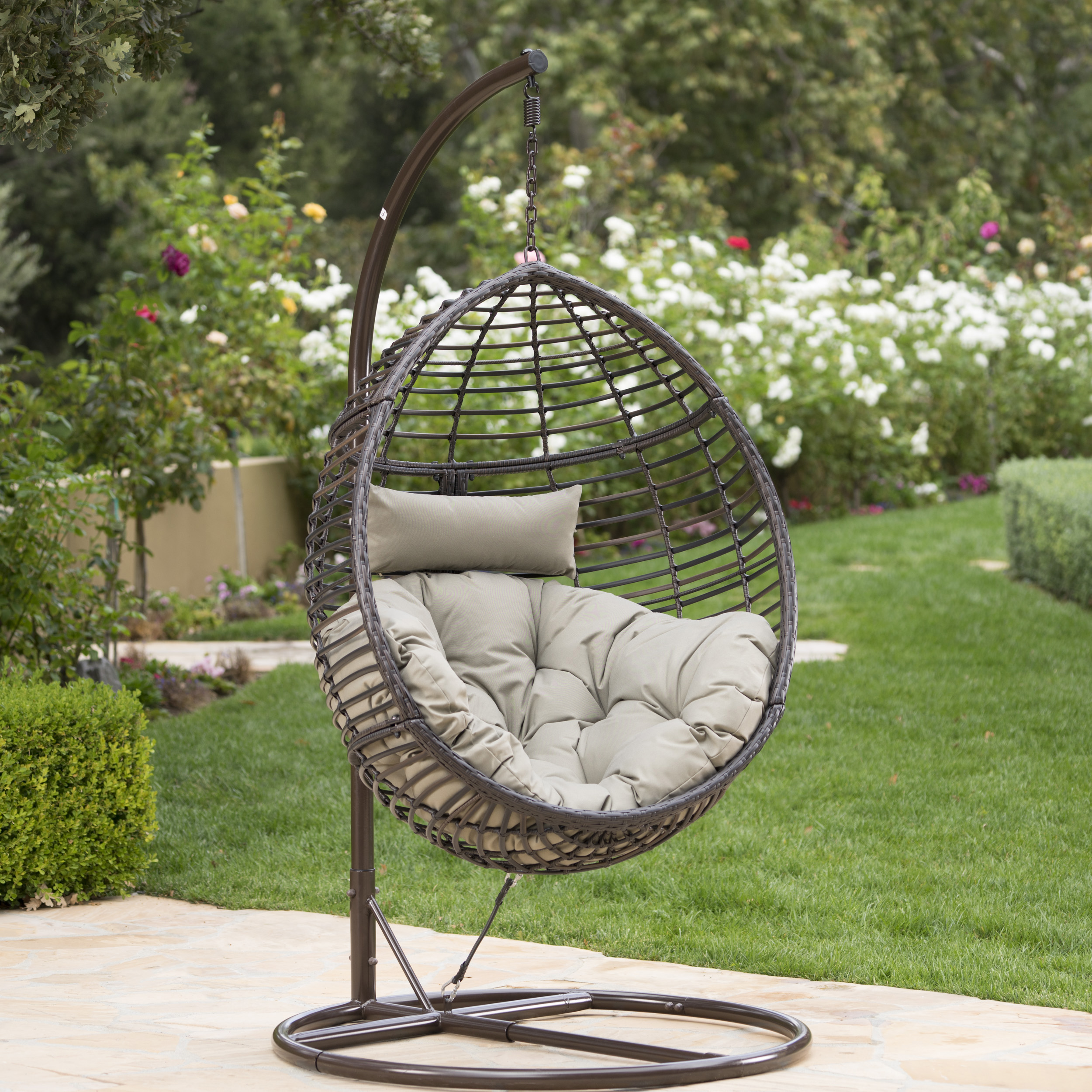 Brown egg-shaped wicker basket with taupe cushion set in a garden