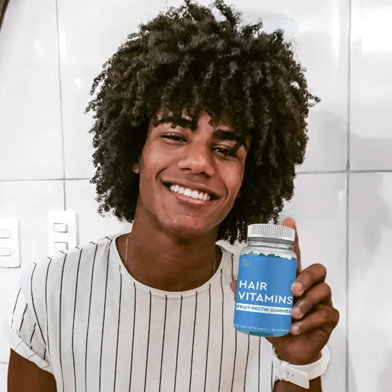 Young man with healthy, full curly hair holding bottle and smiling in casual setting