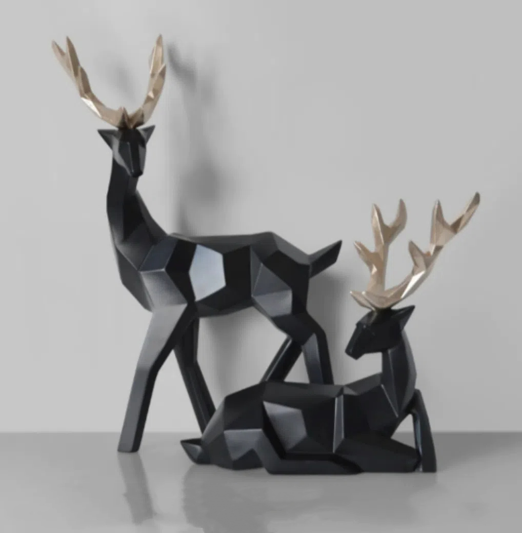 Black standing and seated resin deer pair with gold antlers on grey
